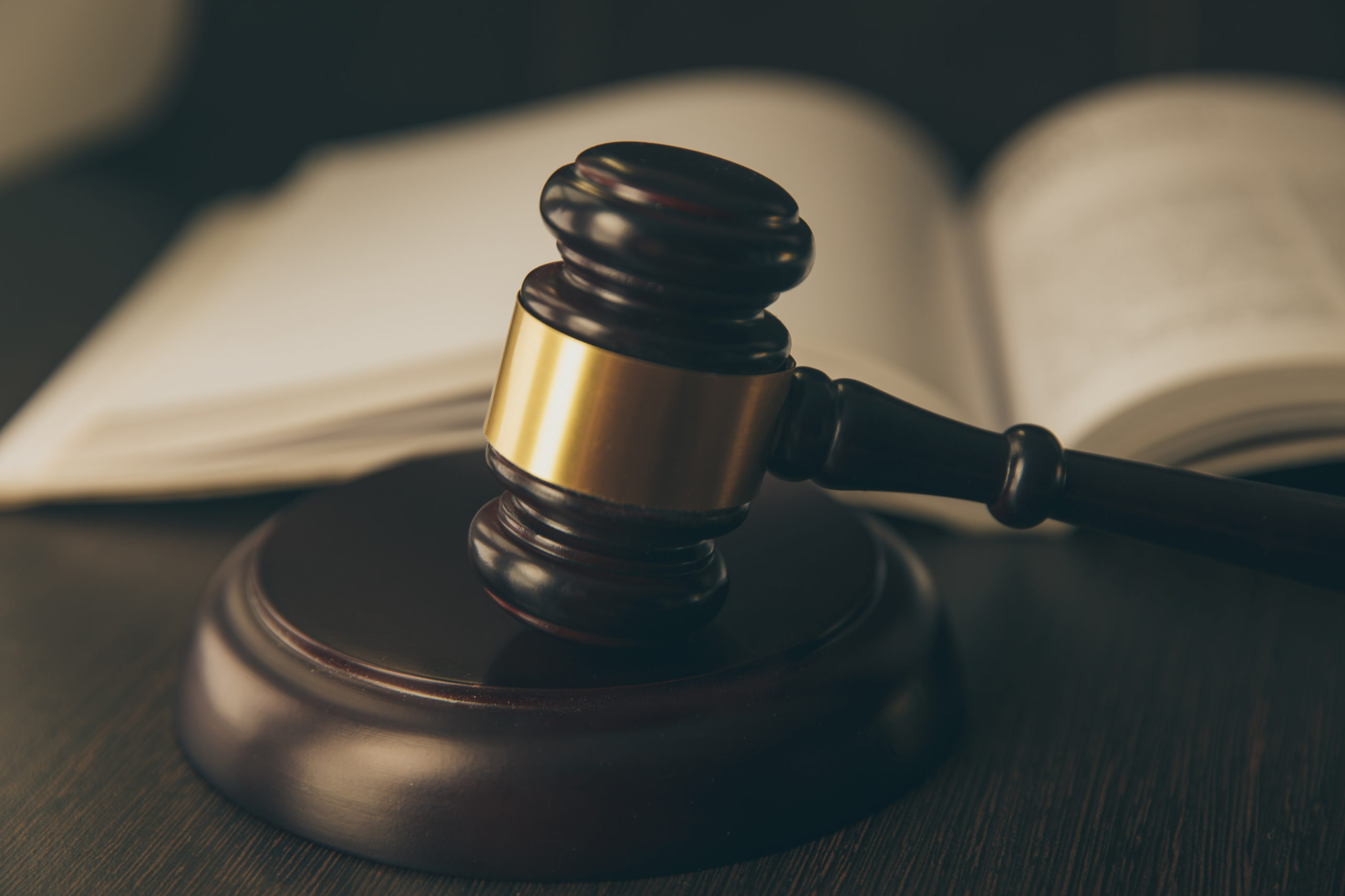 法律概念-打开法律书籍，在法庭或执法办公室的桌子上放一个木制法官木槌，背景为蓝色。